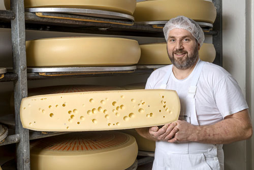 Käsermeister mit einem 
    halben Laib Emmentaler Käse