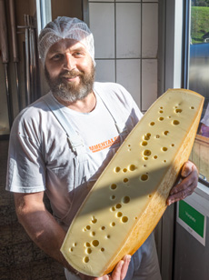 Käsermeister mit halbiertem Käselaib auf dem Arm